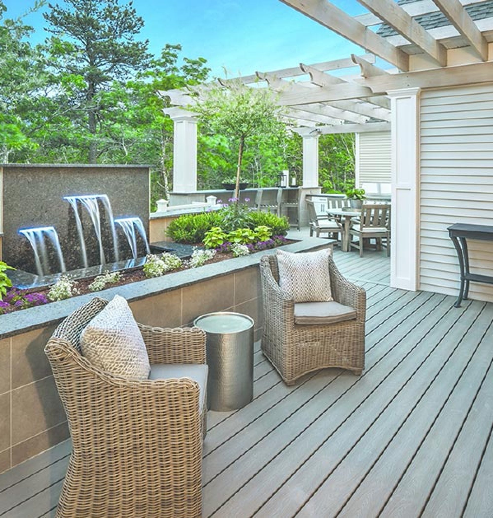 Custom Deck | Custom designed deck with tan deck furniture with raised designed garden and water feature with more deck furniture behind | Backyard Creations | Custom Decks, Porches, and Pergolas